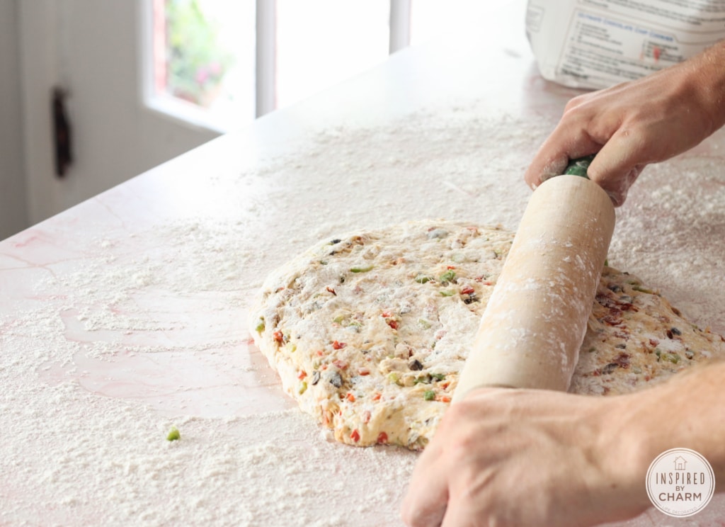 person rolling out pizza dough with a wooden rolling pin