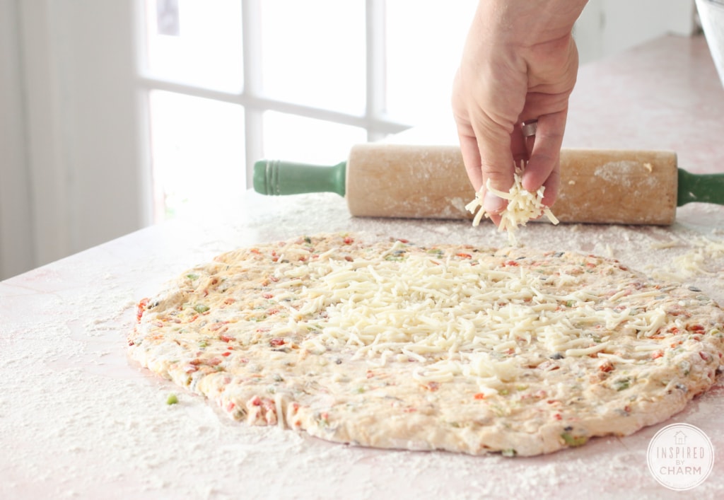 cheese being sprinkled onto rolled out dough