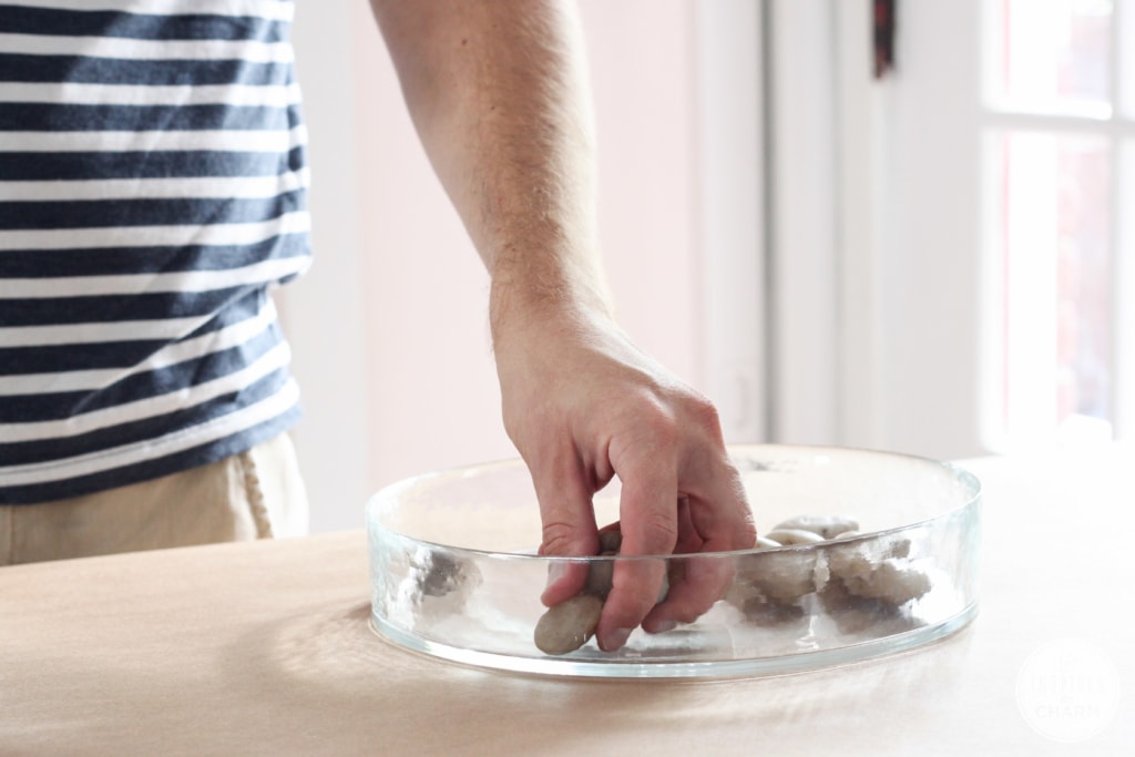 hand adding rocks to a shallow glass dish.