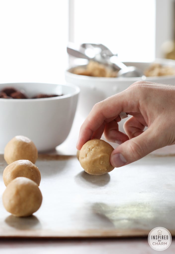 hand placing roll peanut butter cookie dough onto a baking sheet.