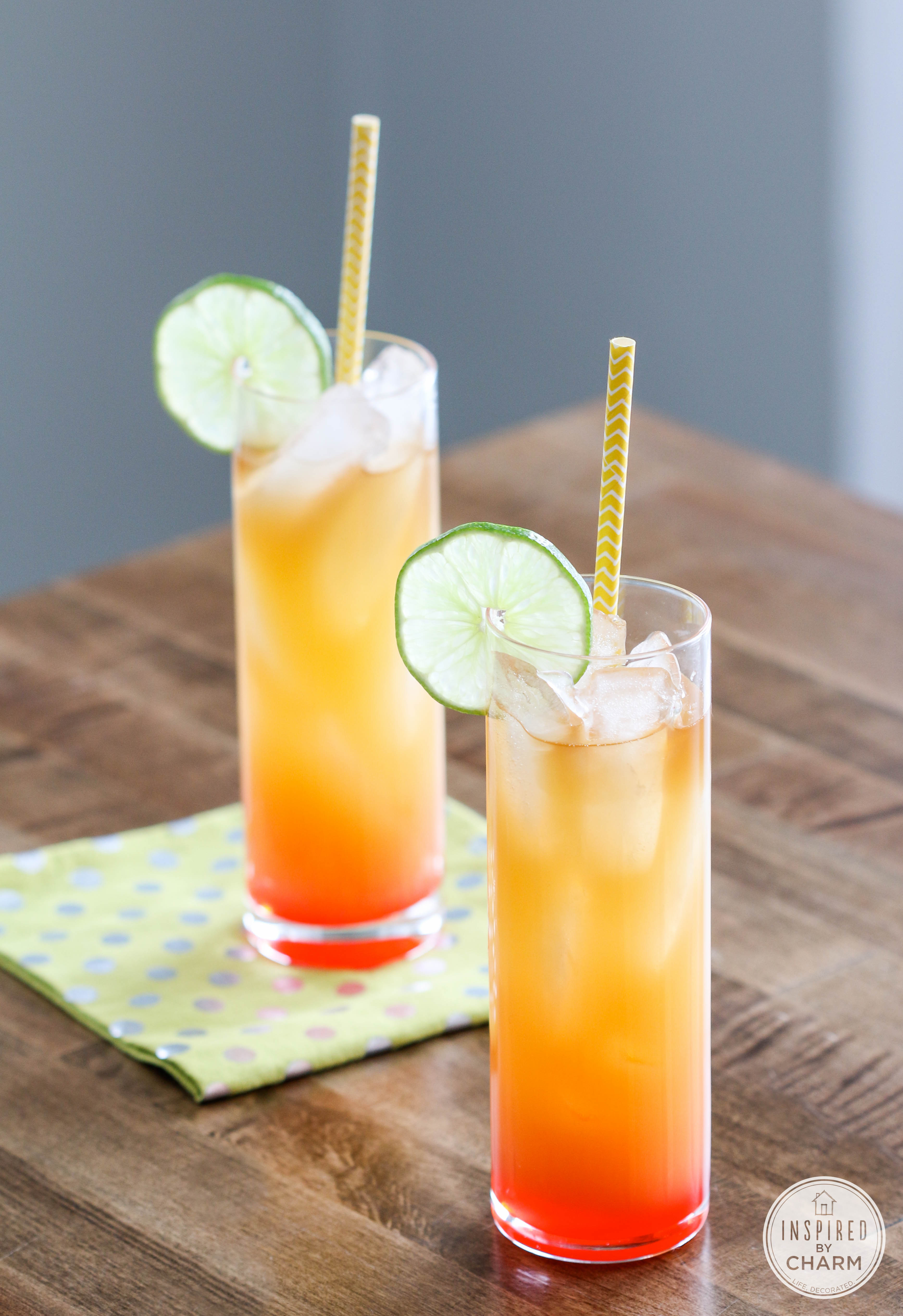 two glasses of rum punch with paper straw and lime wheel garnish.