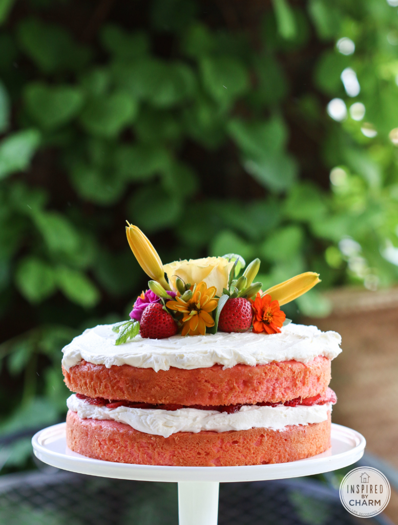 Stunning Strawberry Rhubarb Cake on a cake stand decorated with flowers.