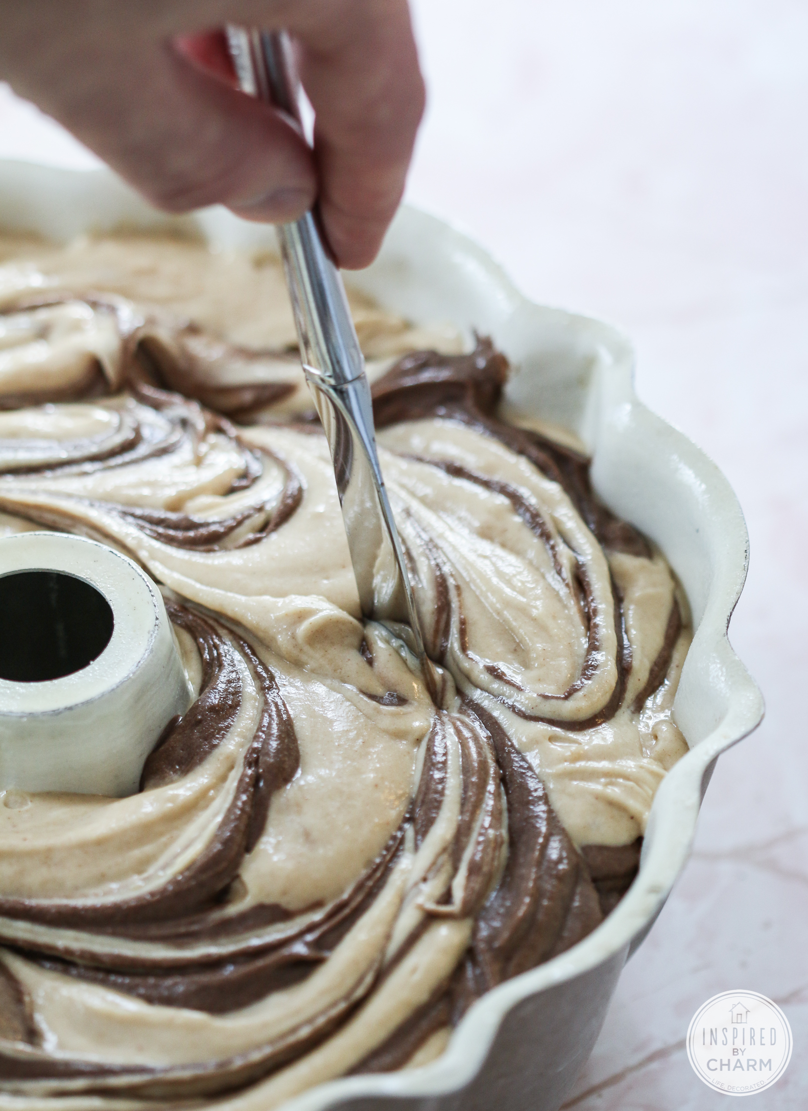 butter knife swirling together peanut butter cake batter and chocolate cake batter in a bundt pan.