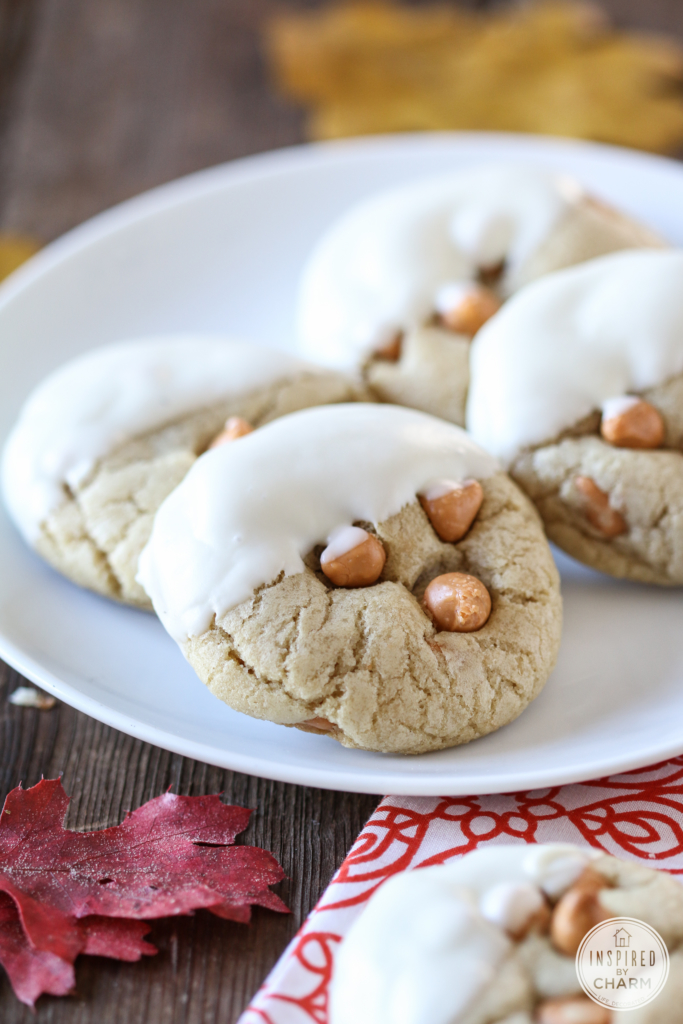 soft-batch Butterscotch Cookies dipped in white chocolate and stacked on a white plate with fall leaves around.