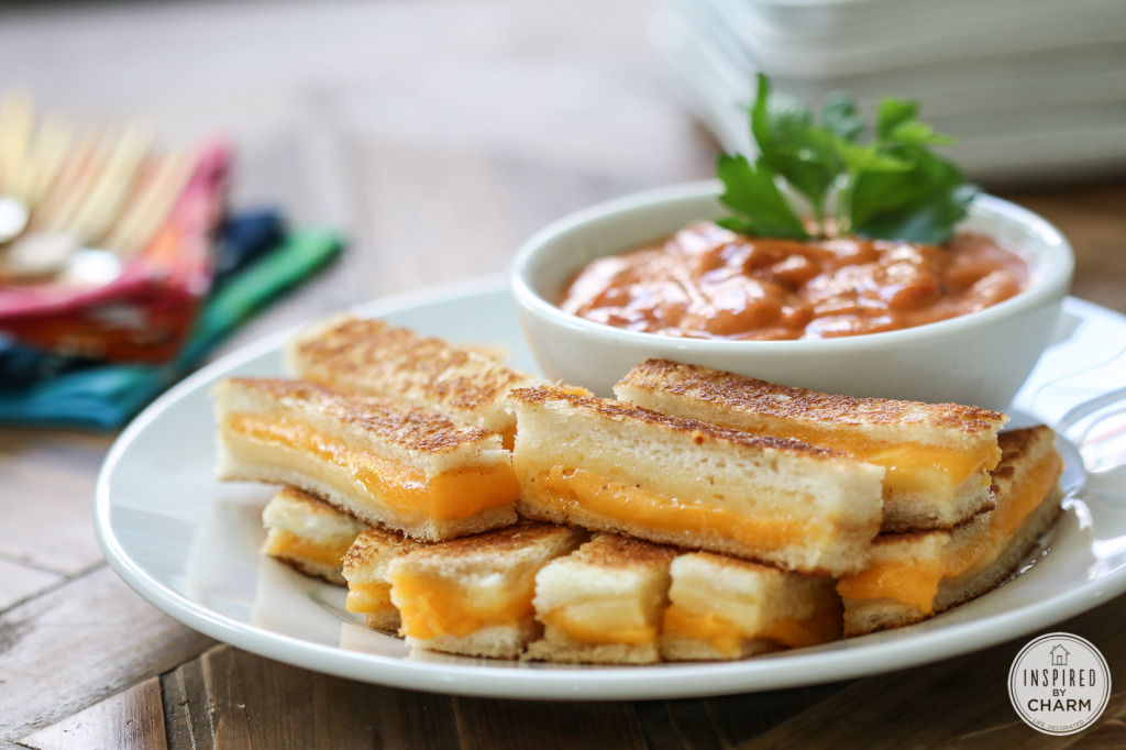 strips of mini grilled cheese on a plate with a bowl of tomato soup. 