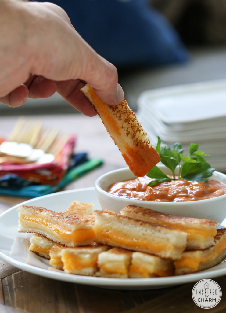 hand dipping mini grilled cheese strip into tomato soup. 