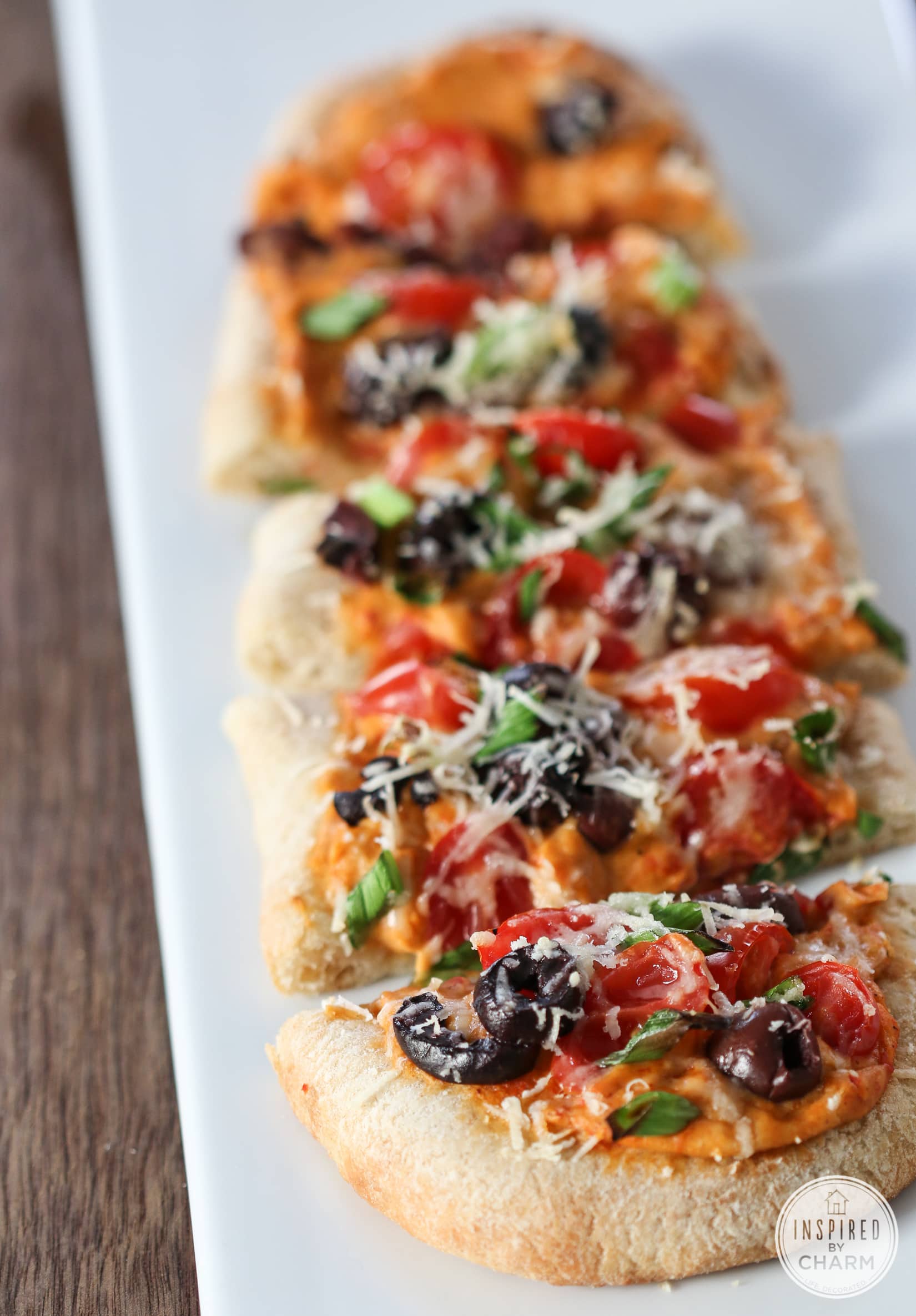 Flatbread topped with hummus, olives, tomatoes, green onions, and cheese