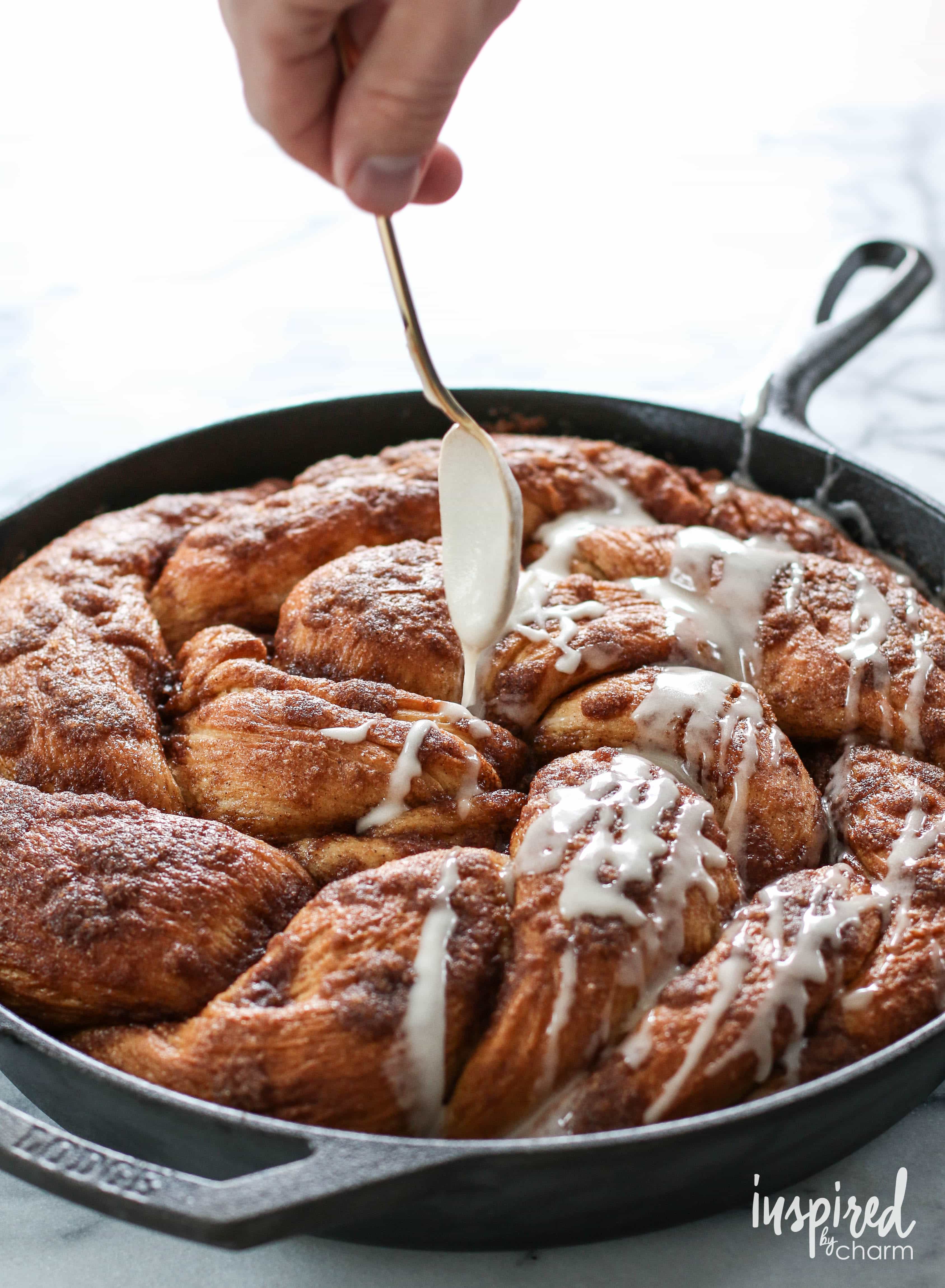 hand with spoon drizzling glaze onto Cinnamon Roll Skillet Bread.