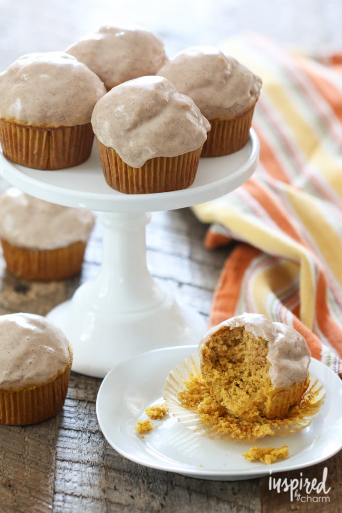 glazed pumpkin donut muffins on a cake stand and one on a plate with a bite removed.