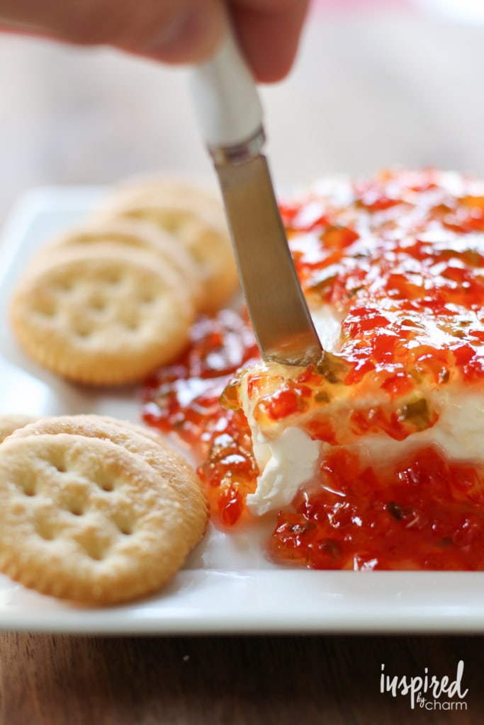cheese knife cutting into block of cream cheese smothered in red pepper jelly