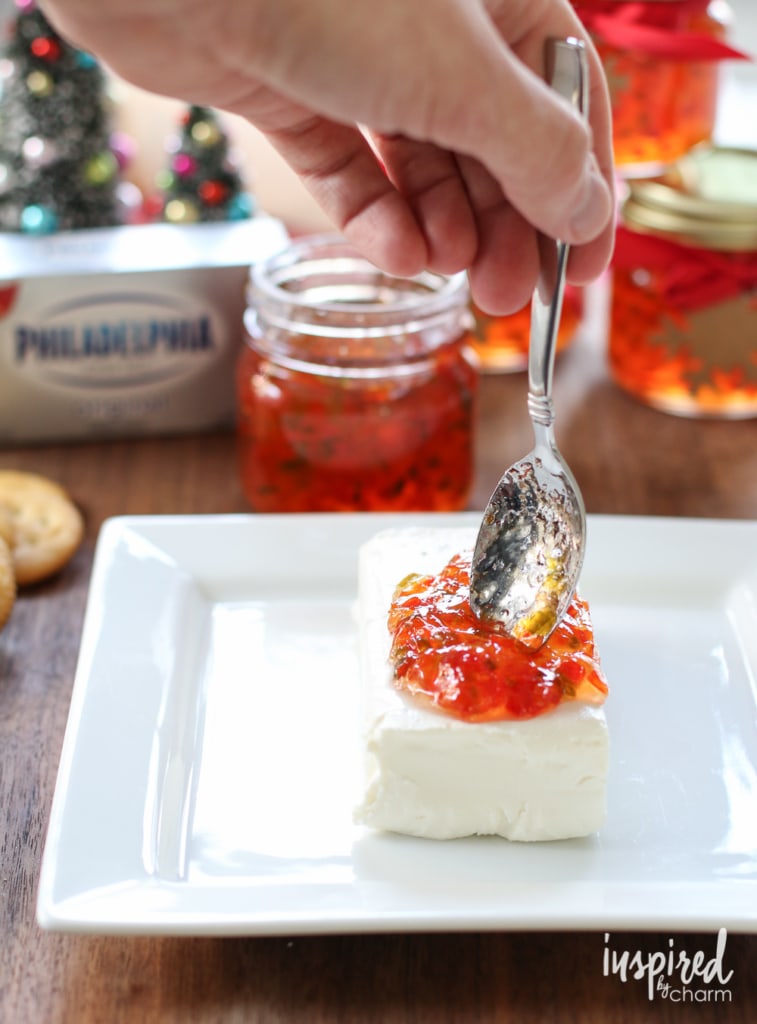 spoonful of pepper jelly being added on top of a block of cream cheese