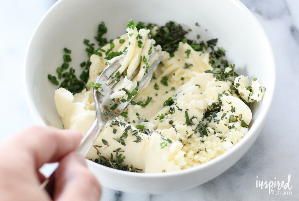 Mashing butter and fresh herbs with a fork to create her butter 