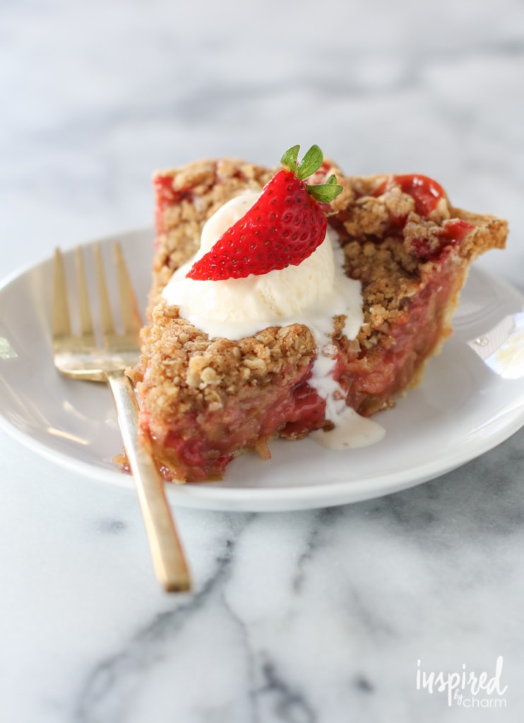 slice of  strawberry rhubarb crumble pie on a plate with a scoop of ice cream and a fork.