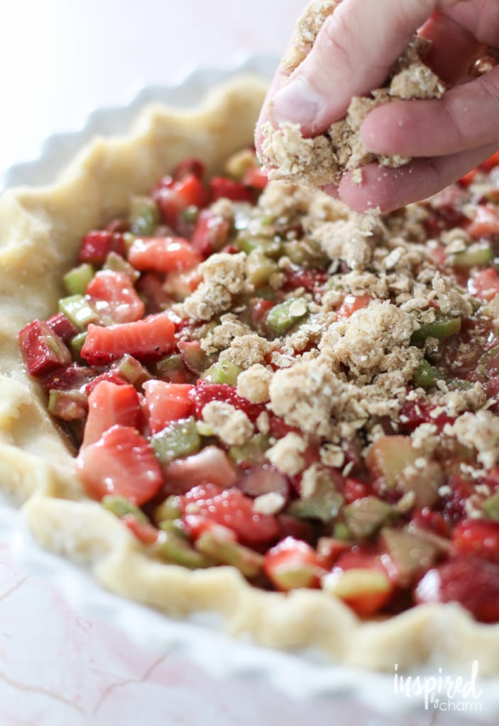 adding crumble topping to a strawberry rhubarb pie.