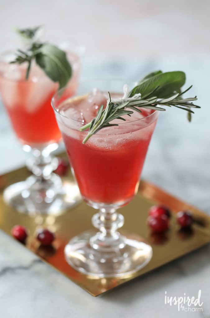 A festive cranberry bourbon cocktail garnished with fresh cranberries, rosemary, and sage, perfect for celebrating the winter season