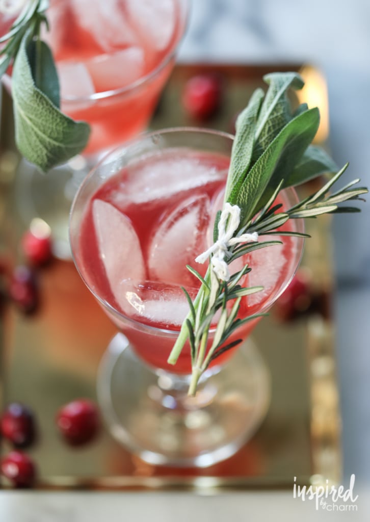 festive cranberry bourbon cocktail in a wine glass, garnished with cranberries and fresh herbsl. The perfect winter drink to celebrate the holiday season!