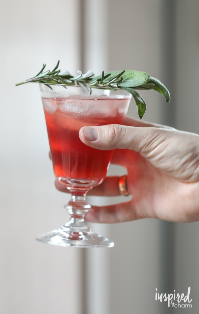 Man holding a cranberry bourbon cocktail with fresh rosemary and sage. 