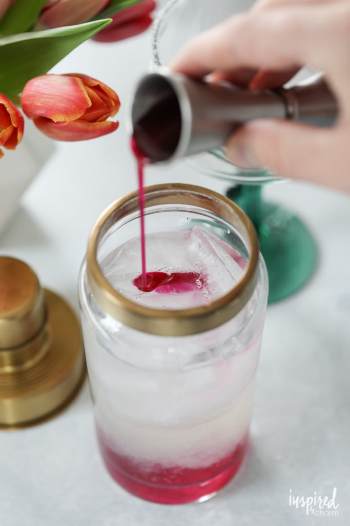 pink syrup being poured into a glass of liquor