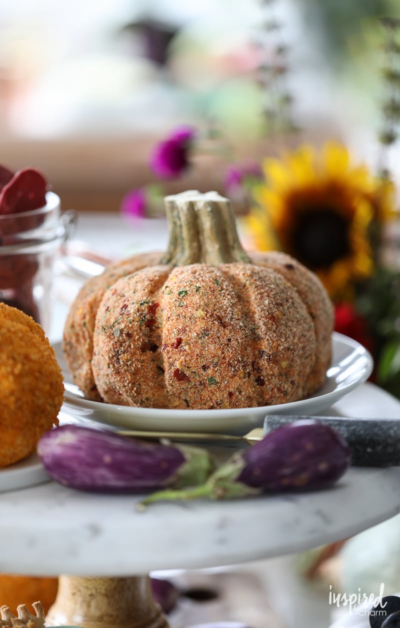 Sun-Dried Tomato Cheeseball on a plate with fall decor around it.