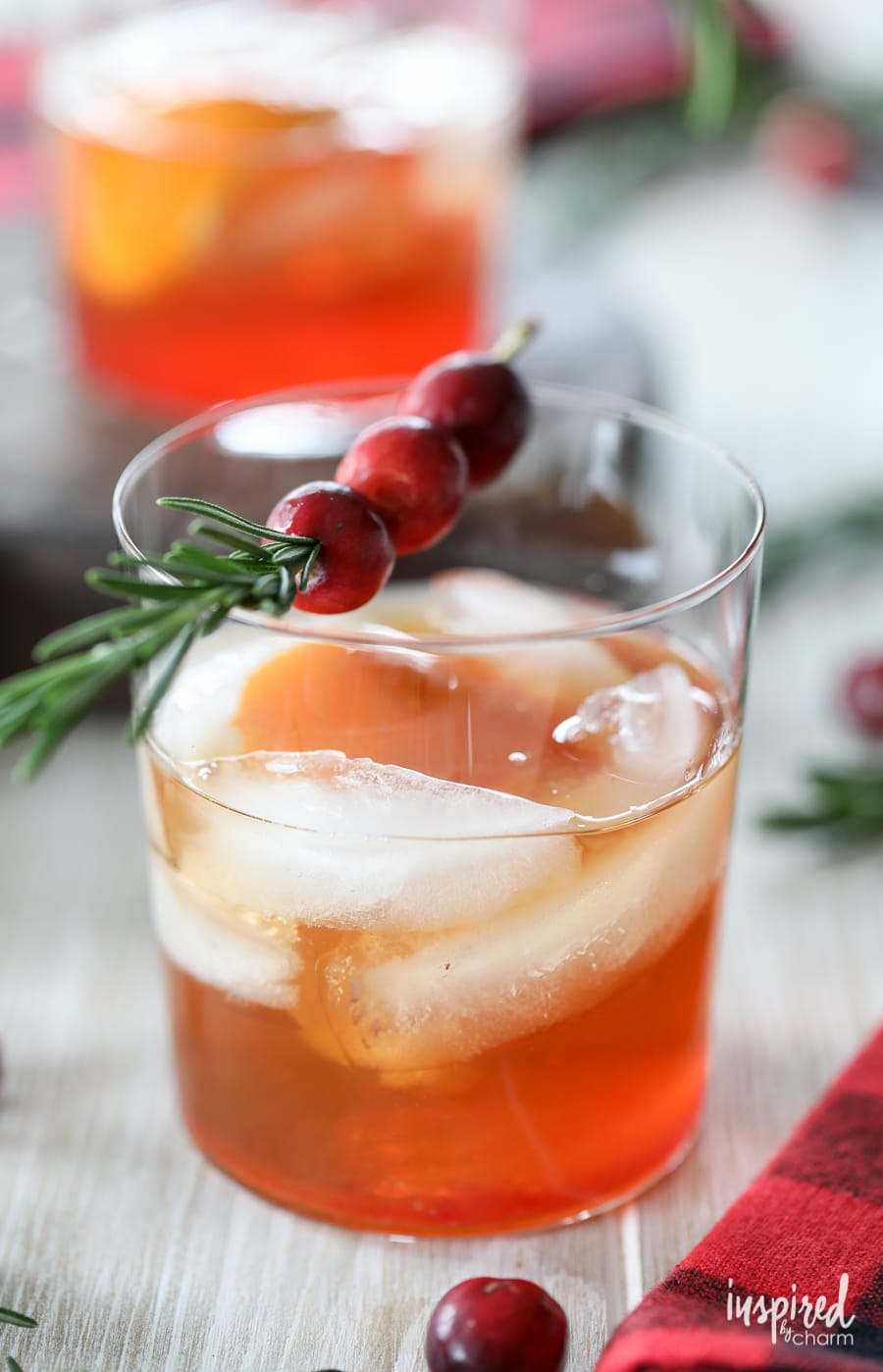 cranberry old fashioned in rocks glass with rosemary and cranberry garnish.