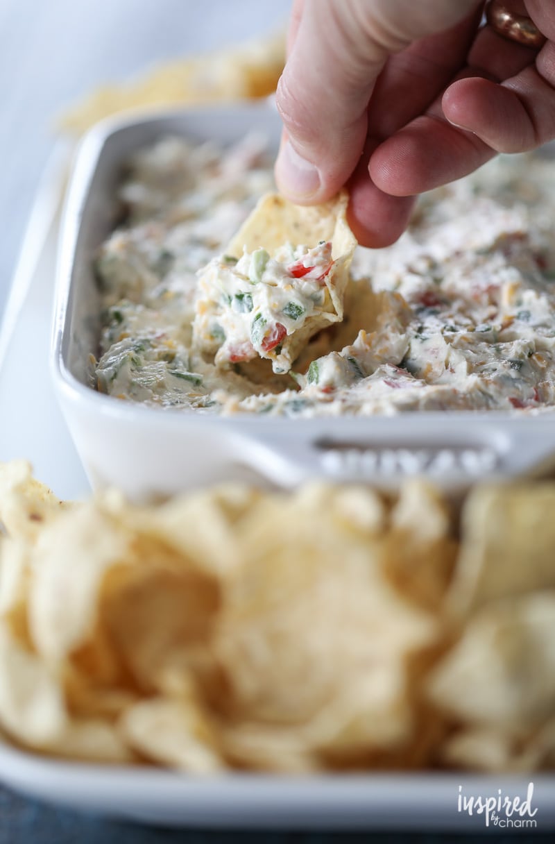 hand stopping  jalapeño dip in a serving dish with tortilla chips. 
