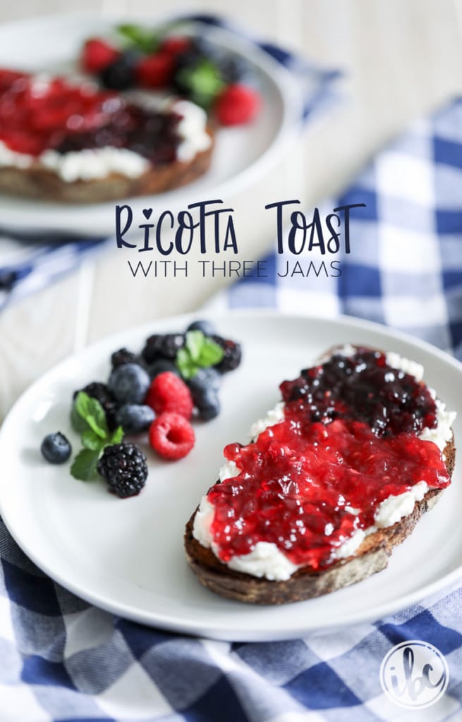 slice of toast spread with ricotta and topped with three berry jams on a plate with fresh berries with another plate in the background.