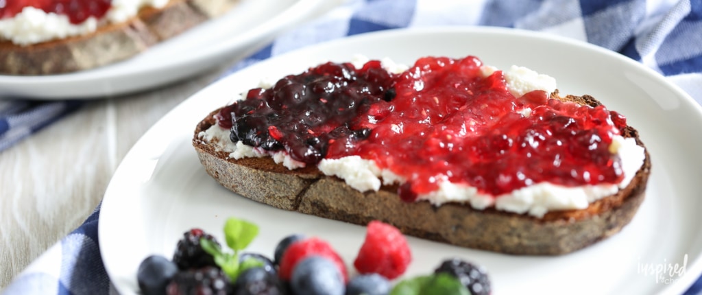 slice of toast spread with ricotta and topped with three berry jams on a plate with fresh berries.