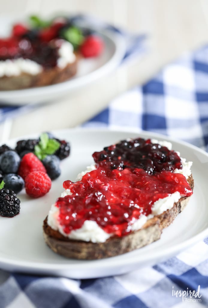 toasted bread with fresh ricotta and jam served on a plate with fresh berries.