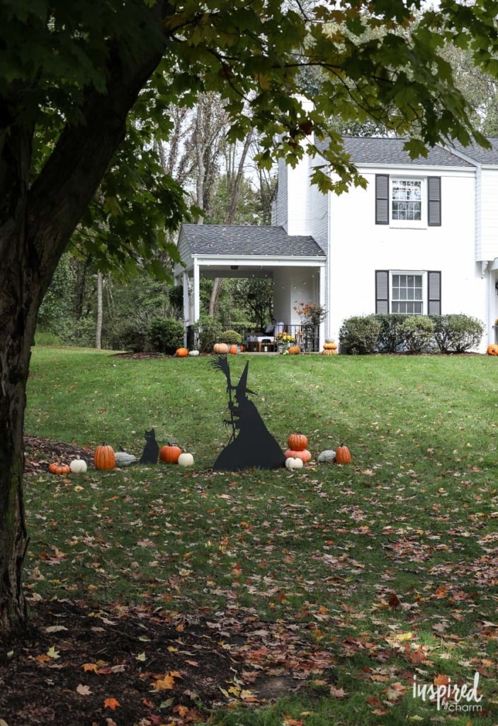 silhouette of a witch and cat and assorted pumpkins in a front yard