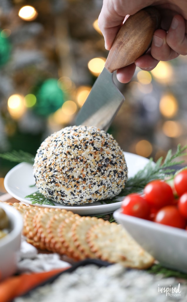 a knife cutting into a cheeseball coated with everything bagel seasoning