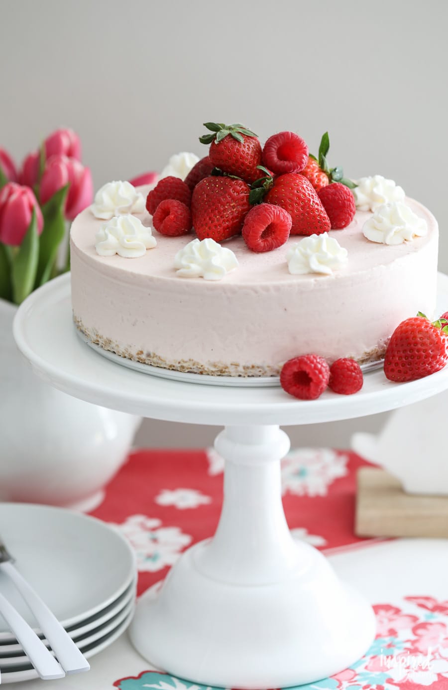 strawberry ice cream cheesecake on a cake stand topped with fresh berries.