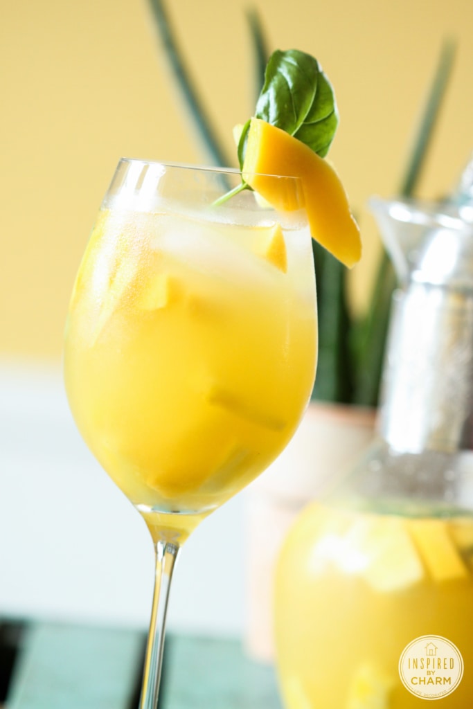 pineapple mango sangria in a glass with mango and basil garnish with pitcher of sangria. 