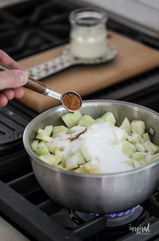adding cinnamon and sugar to granny smith apples in a mixing bowl