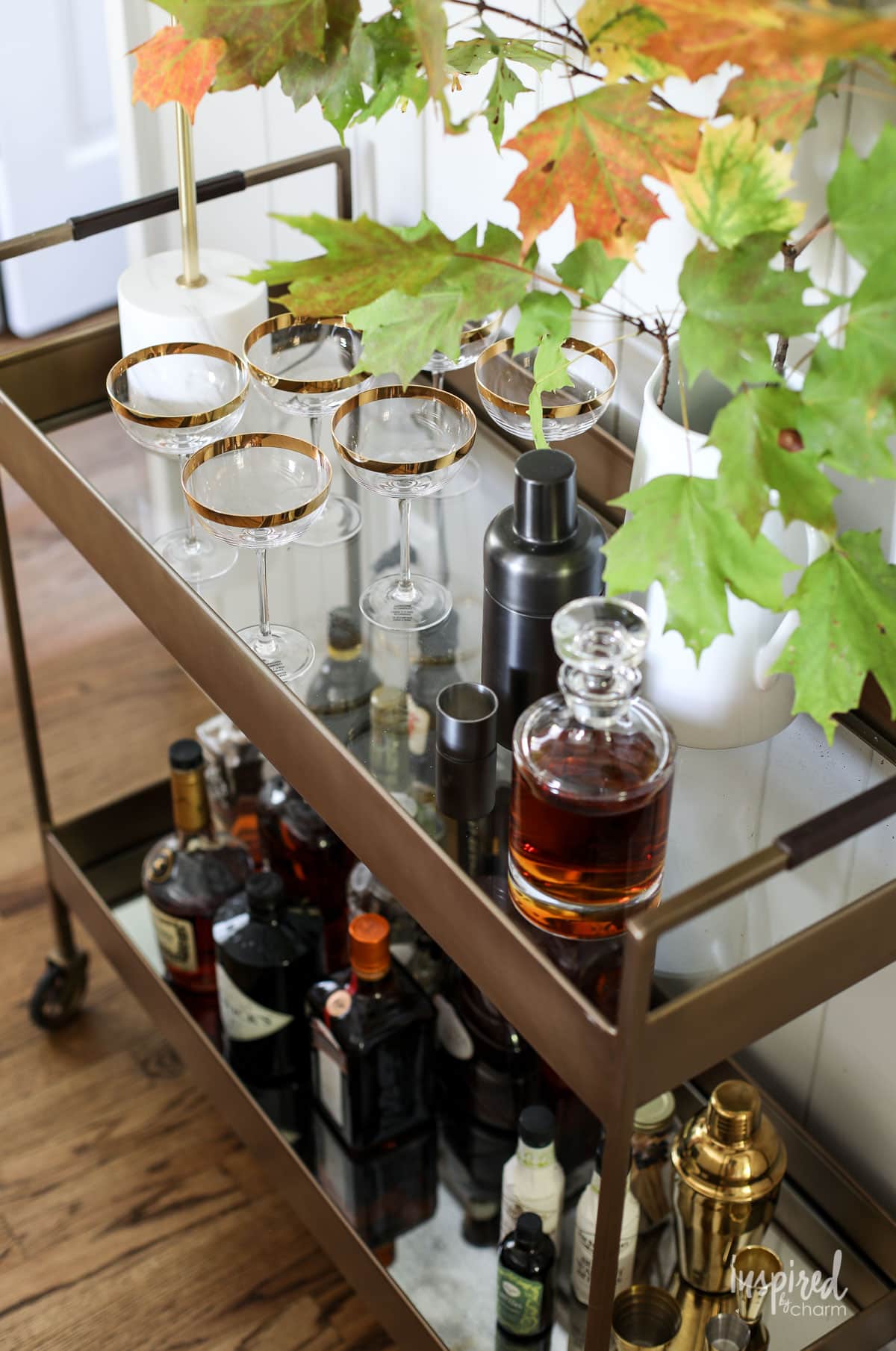 bar cart styled with glassware and a branch of fall leaves.