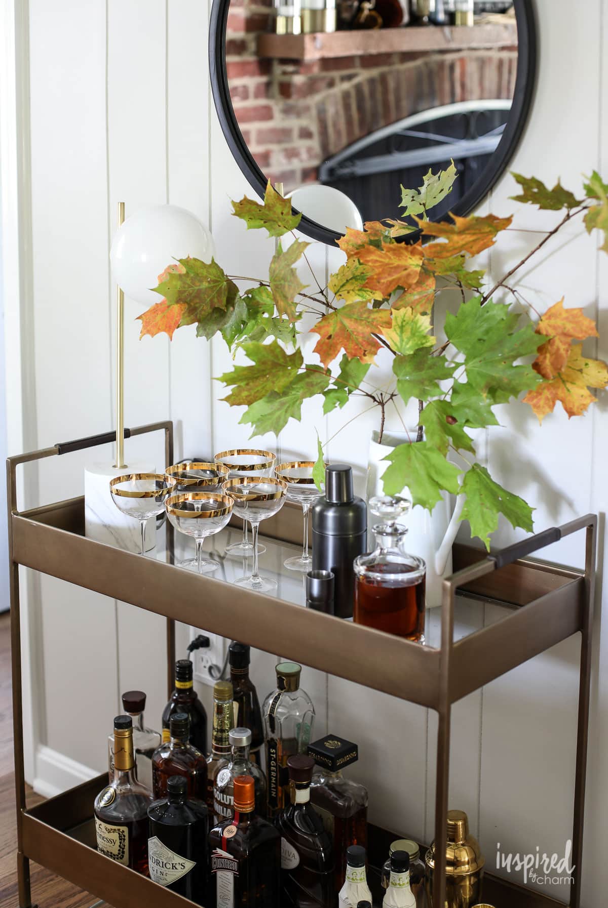 brass bar cart styled with glassware and a branch of fall leaves.