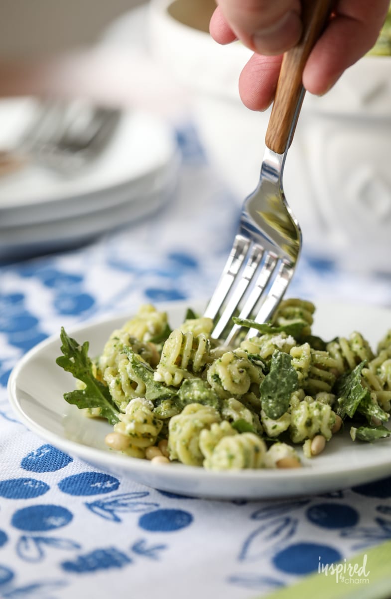 a fork getting a bite of Pine Nut and Arugula Pesto Pasta Salad on a plate.
