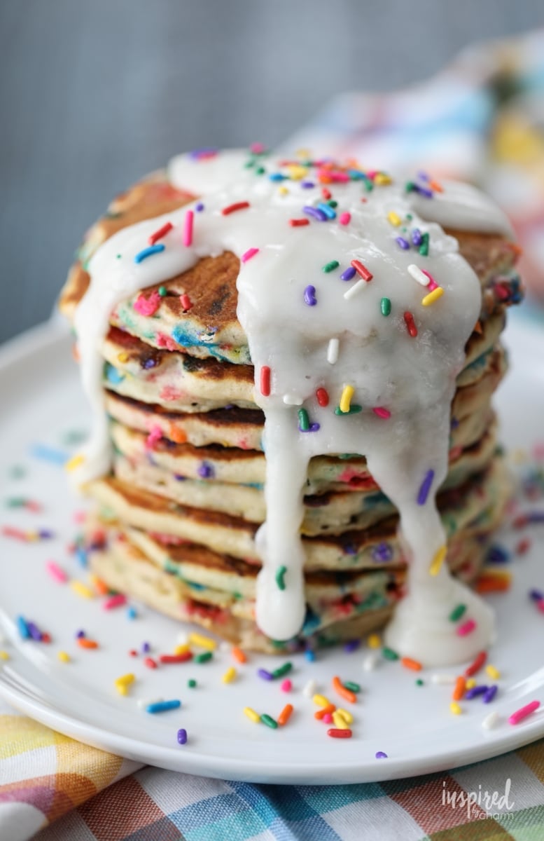 stack of funfetti pancakes drizzled with frosting and topped with sprinkles. 