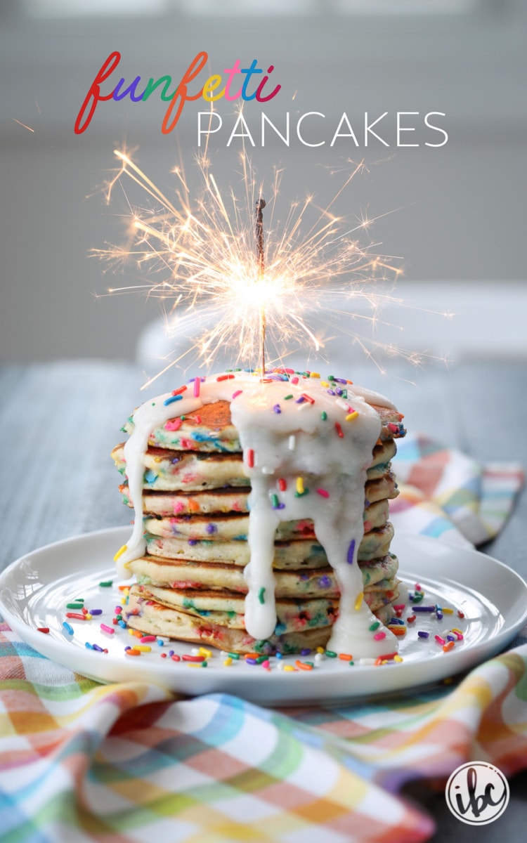stack of funfetti pancakes drizzled with frosting and sprinkles and topped with a sparkler. 