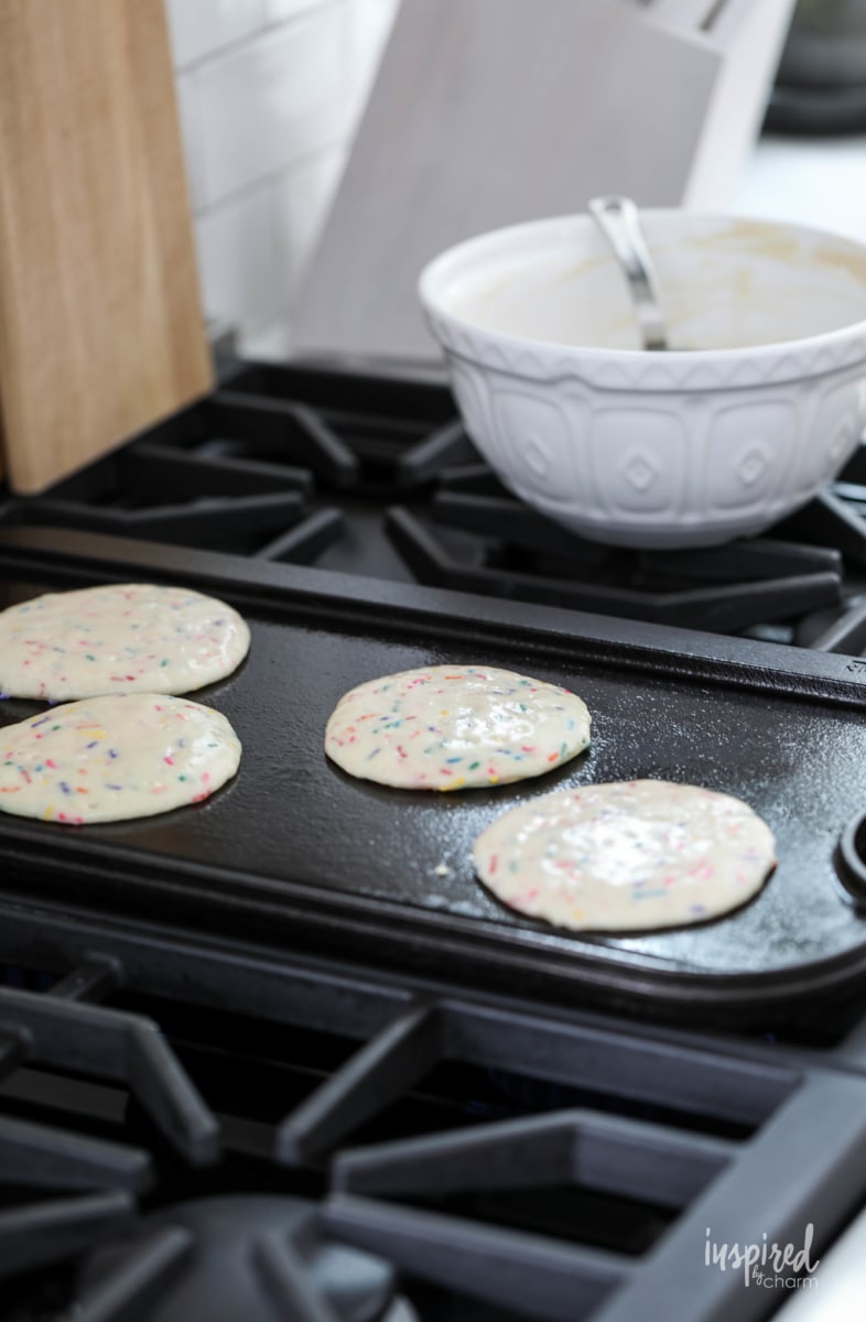 funfetti pancakes cooking on a stovetop griddle.