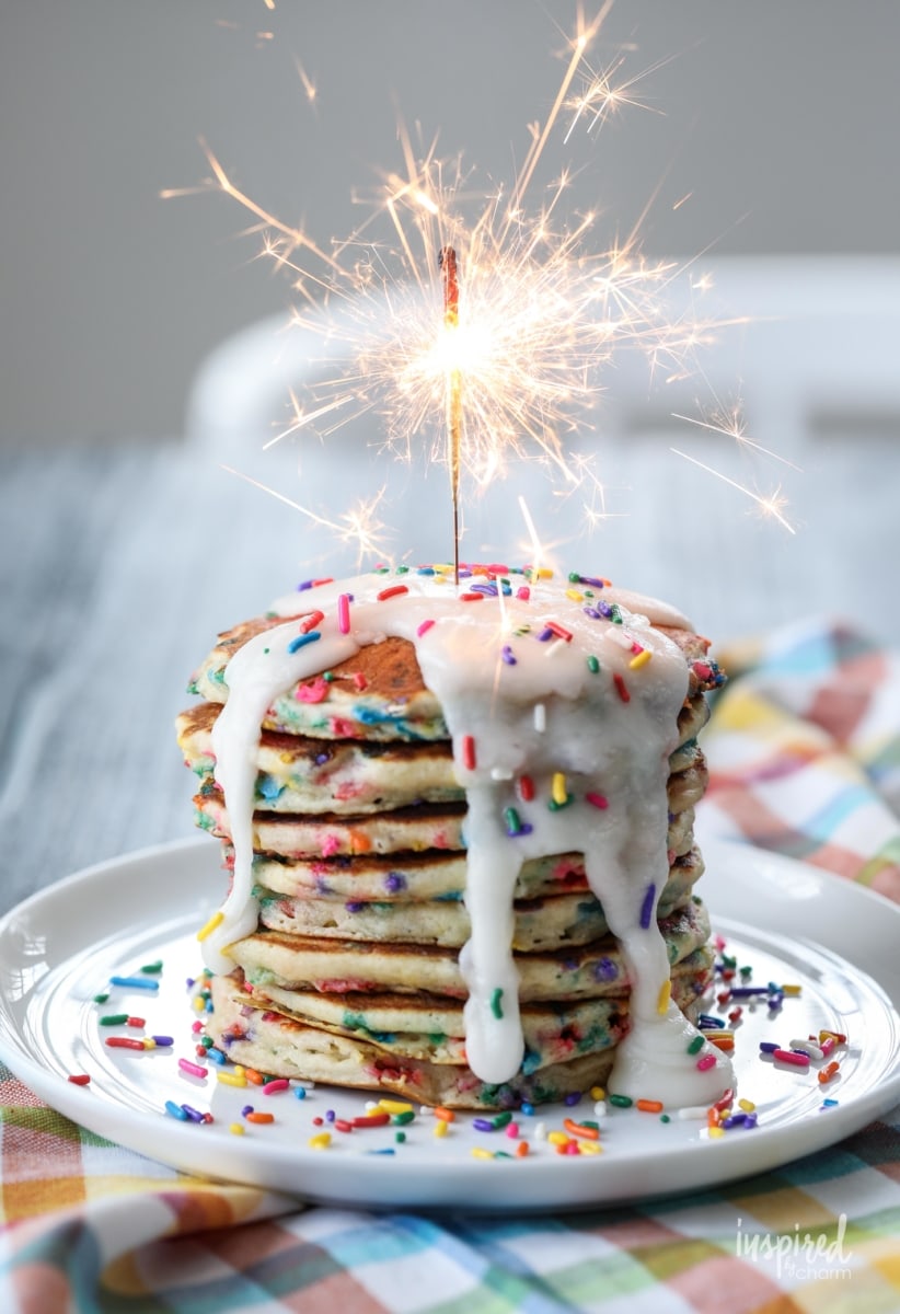 funfetti pancakes stacked with drizzle frosting and a sparkler. 