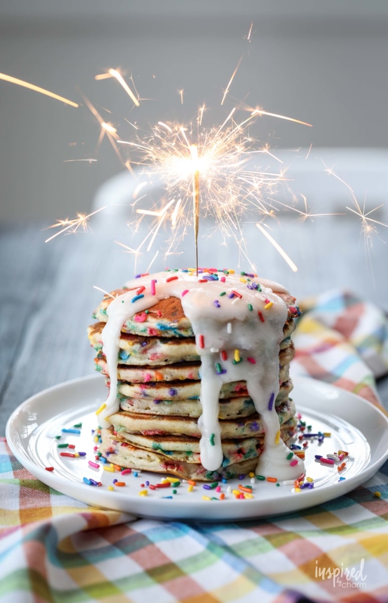 stack of funfetti pancakes with frosting, sprinkles and topped with a sparkler. 