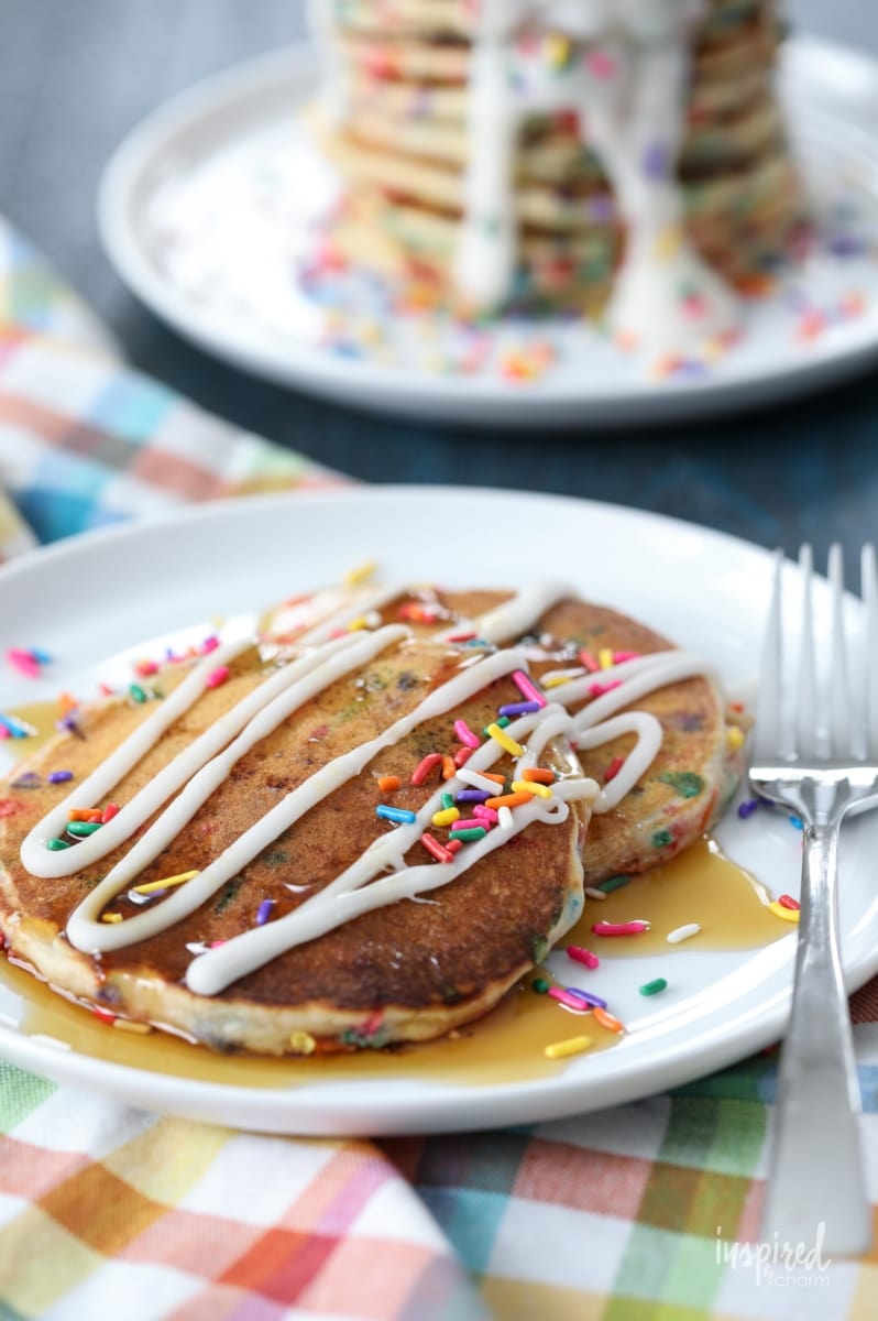 plate of funfetti pancakes topped with a drizzle of frosting, maple syrup and sprinkles.