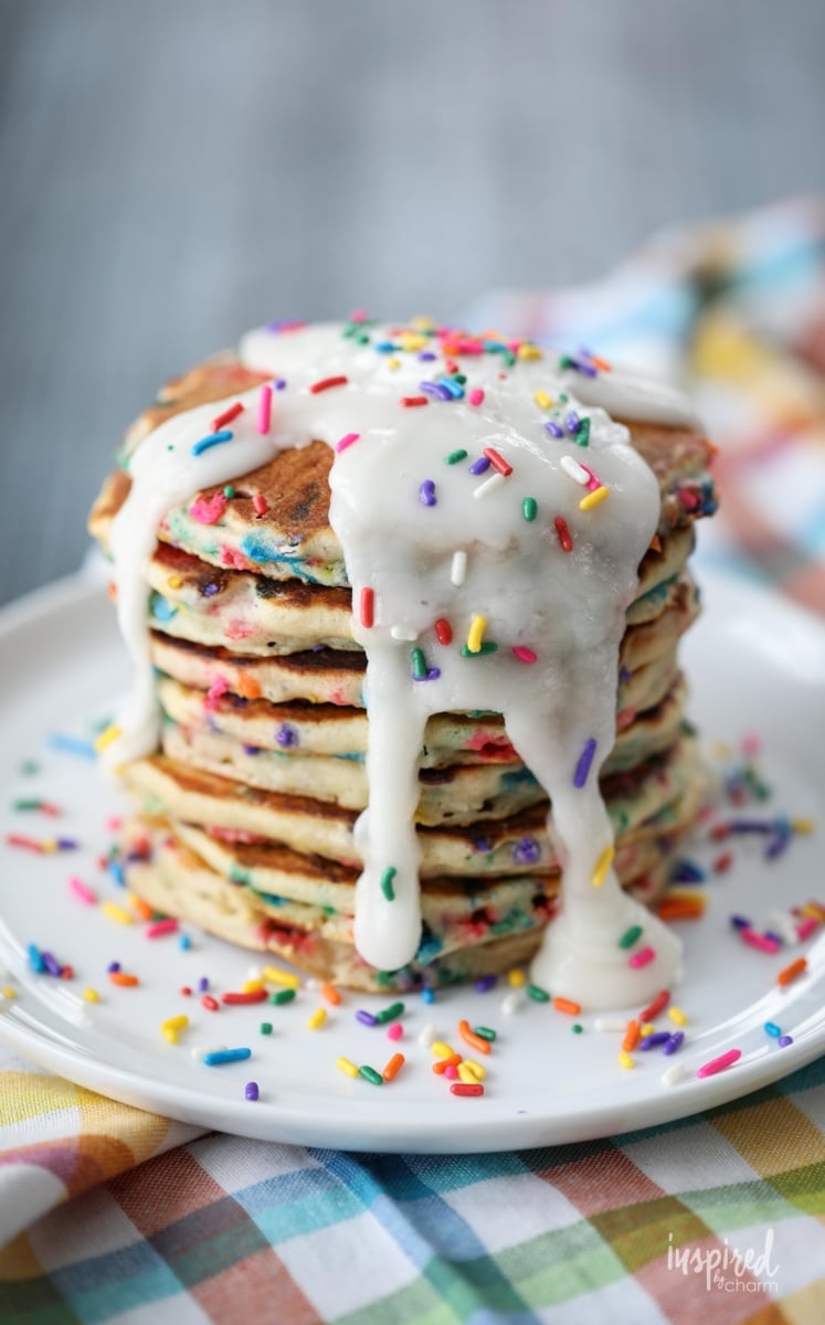 stack of funfetti pancakes topped with frosting and sprinkles. 