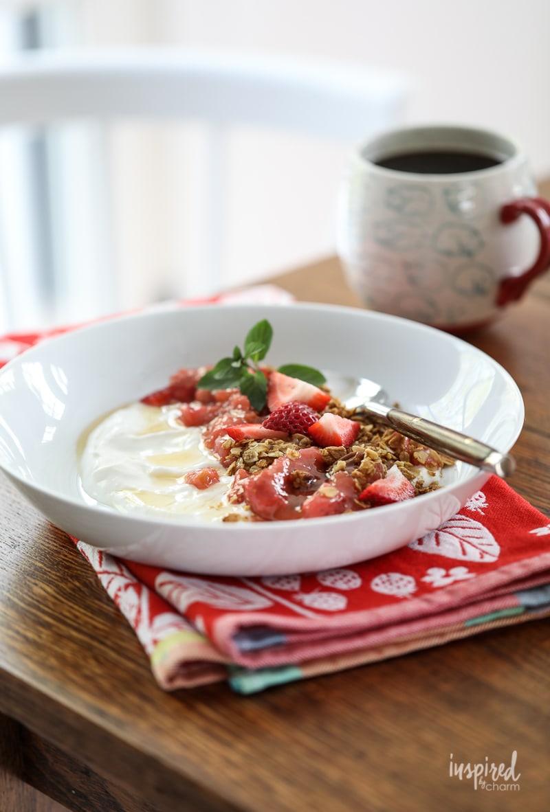Yogurt with Granola, Strawberry, Rhubarb and Honey in a bowl with cup of coffee.