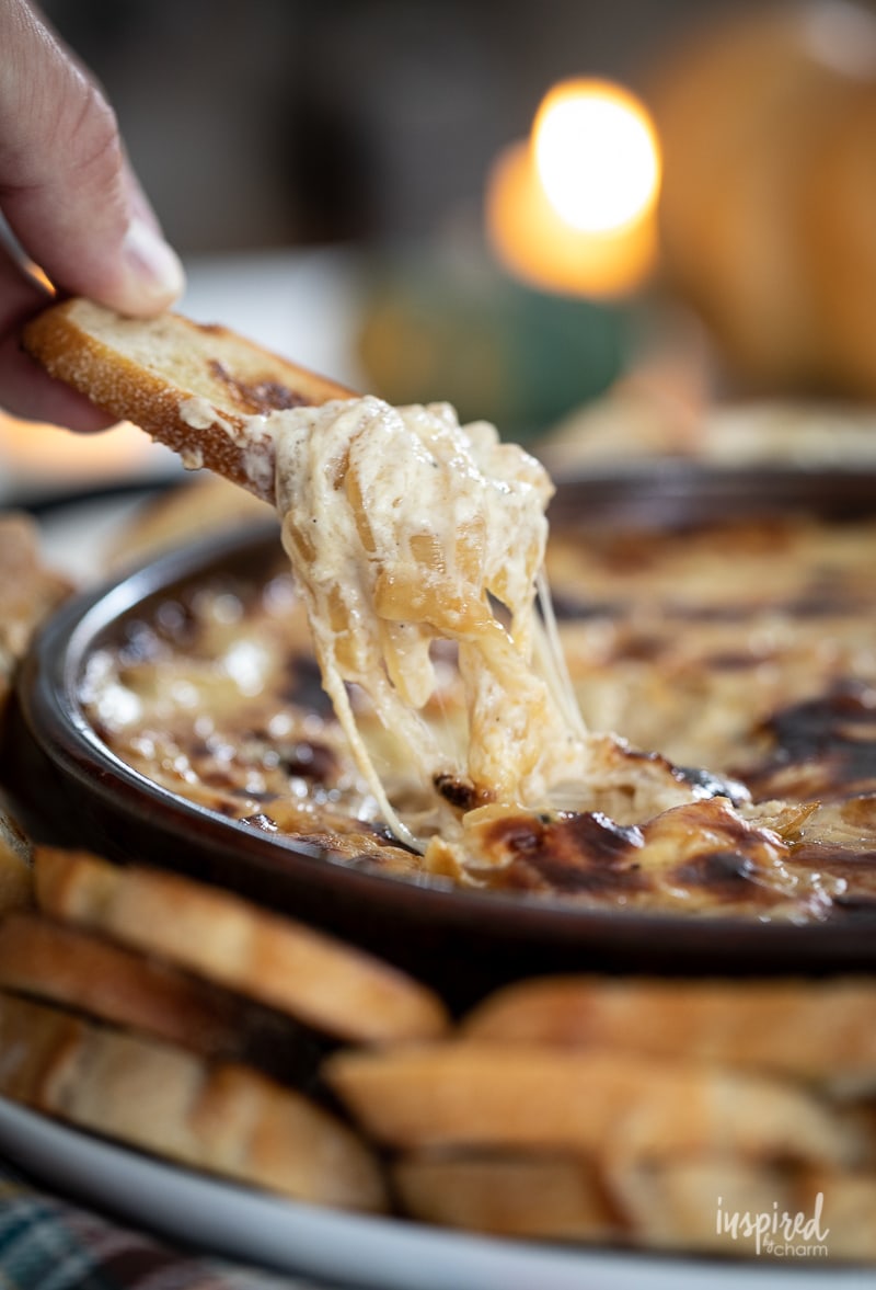 Baked Caramelized Onion Dip in pan with a hand scooping some out with a crostini.
