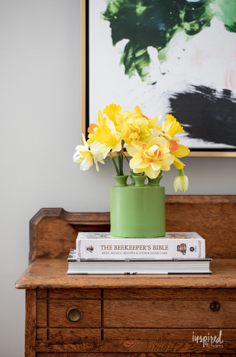 green tulipiere vase filled with daffodils on a stack of books. 