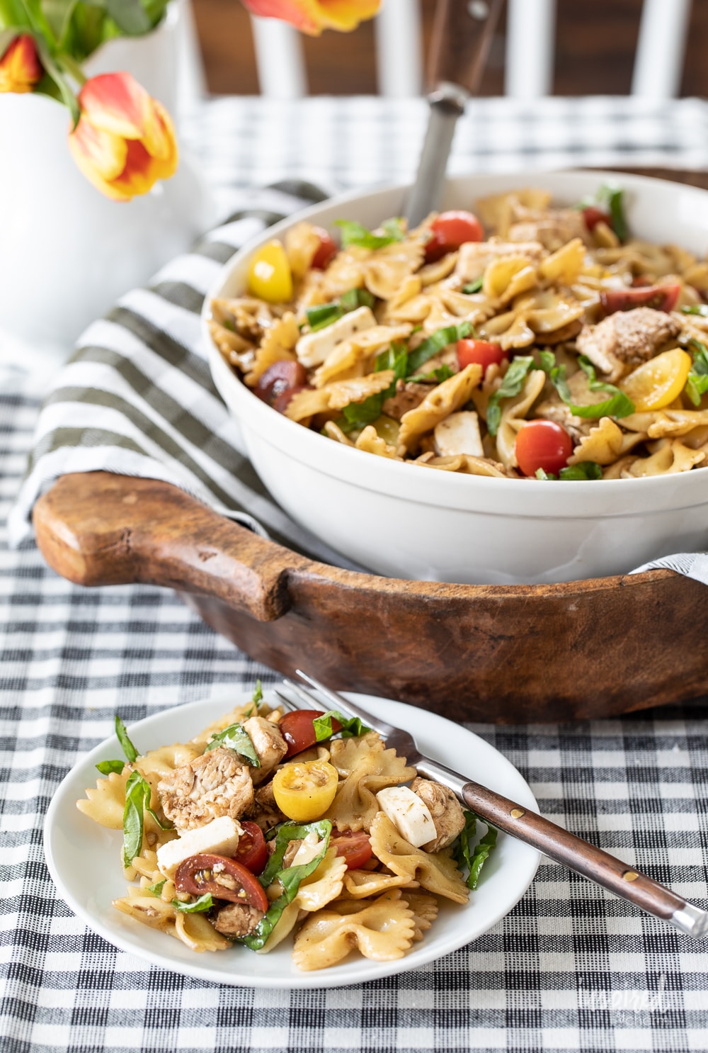 Delicious Chicken Caprese Pasta Salad in a large bowl with a serving on a plate.
