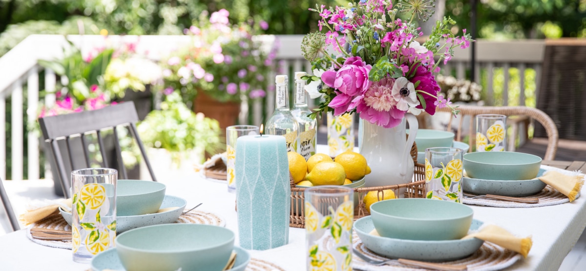 outdoor table setting with flowers, candles, and dinnerware.