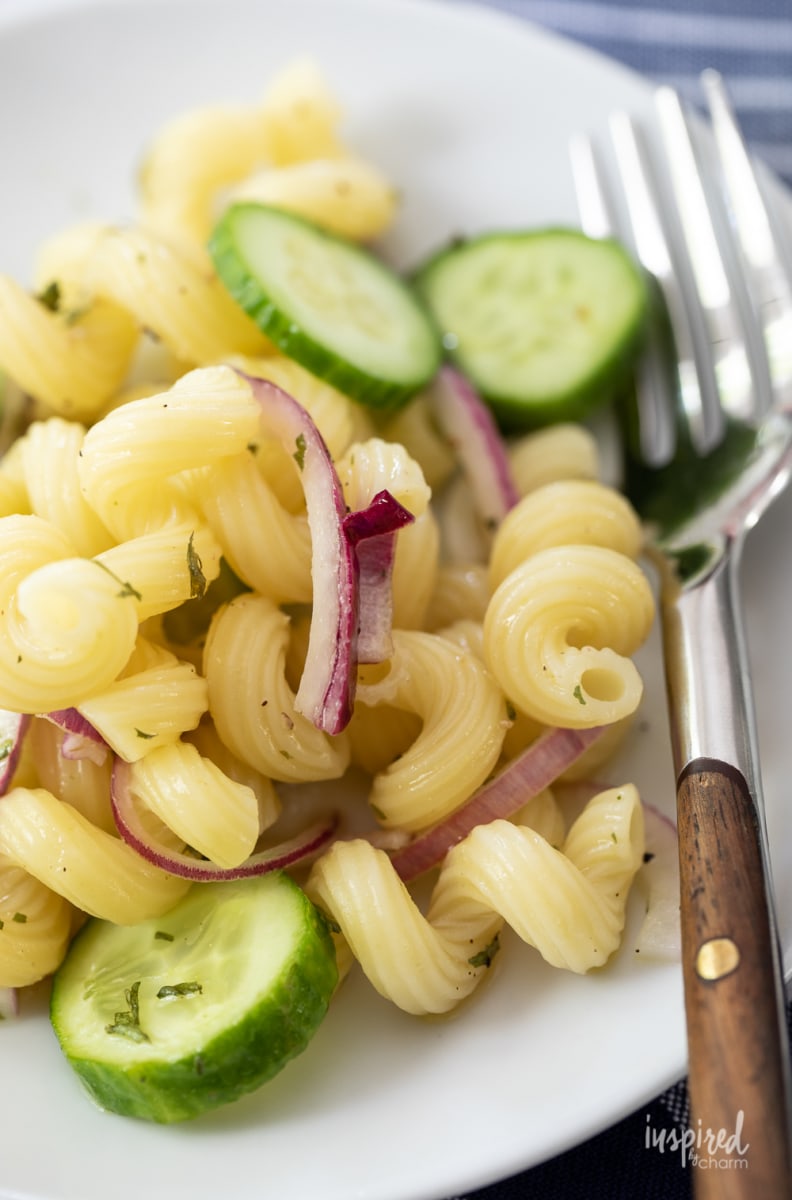 close up of cucumber pasta salad with red onions on a plate with a fork. 
