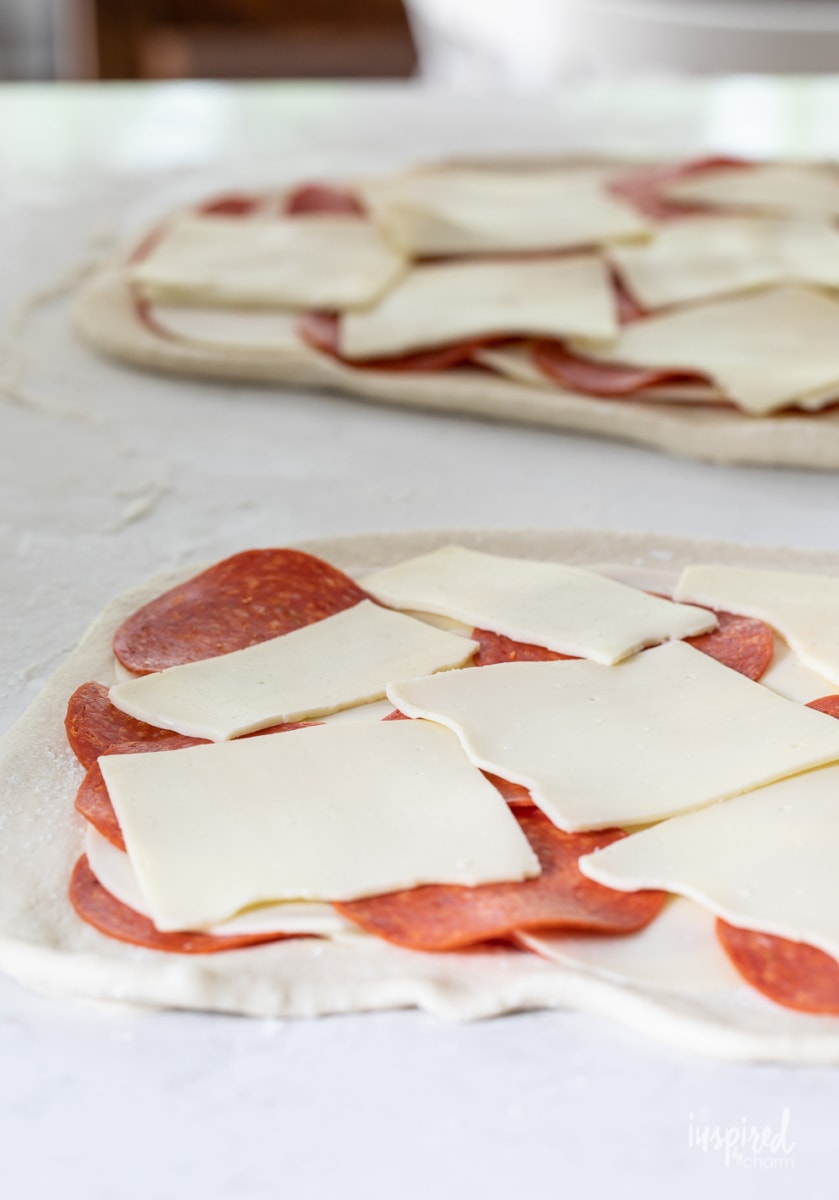 sliced cheese and cured meat on rolled out dough